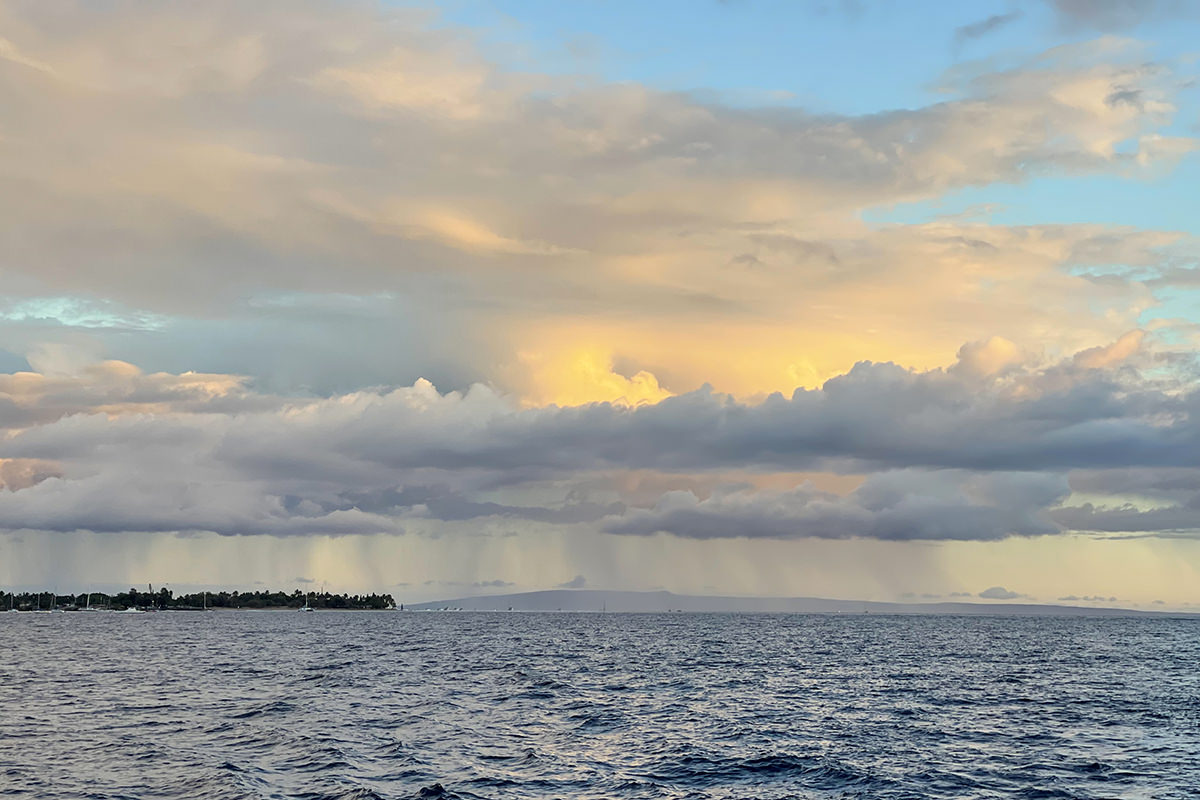 Buttery sun glows through the clouds as rain can be seen pouring in the distance.