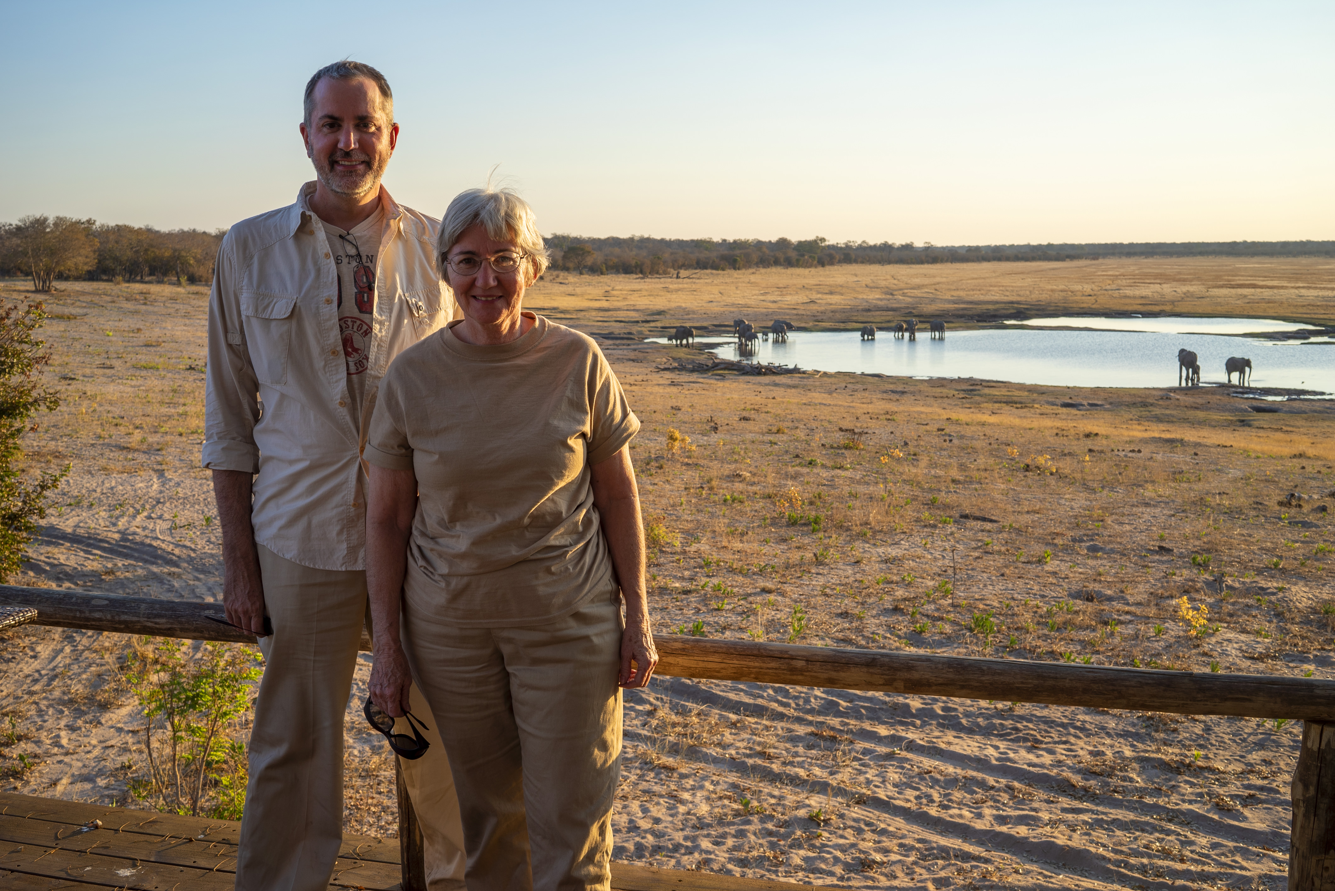 Mom and I in front of a watering hole with elephants around it.