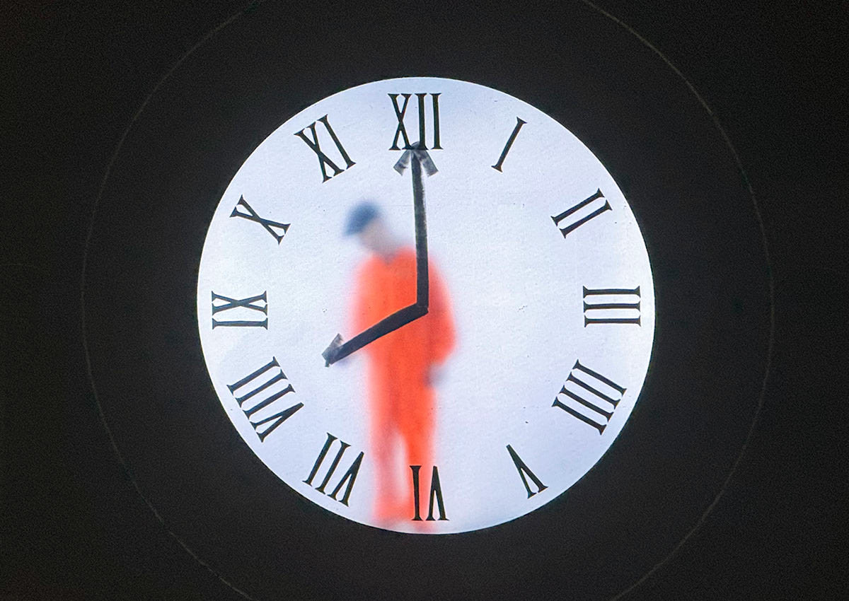 A man behnd a clock face drawing the hands of the clock.