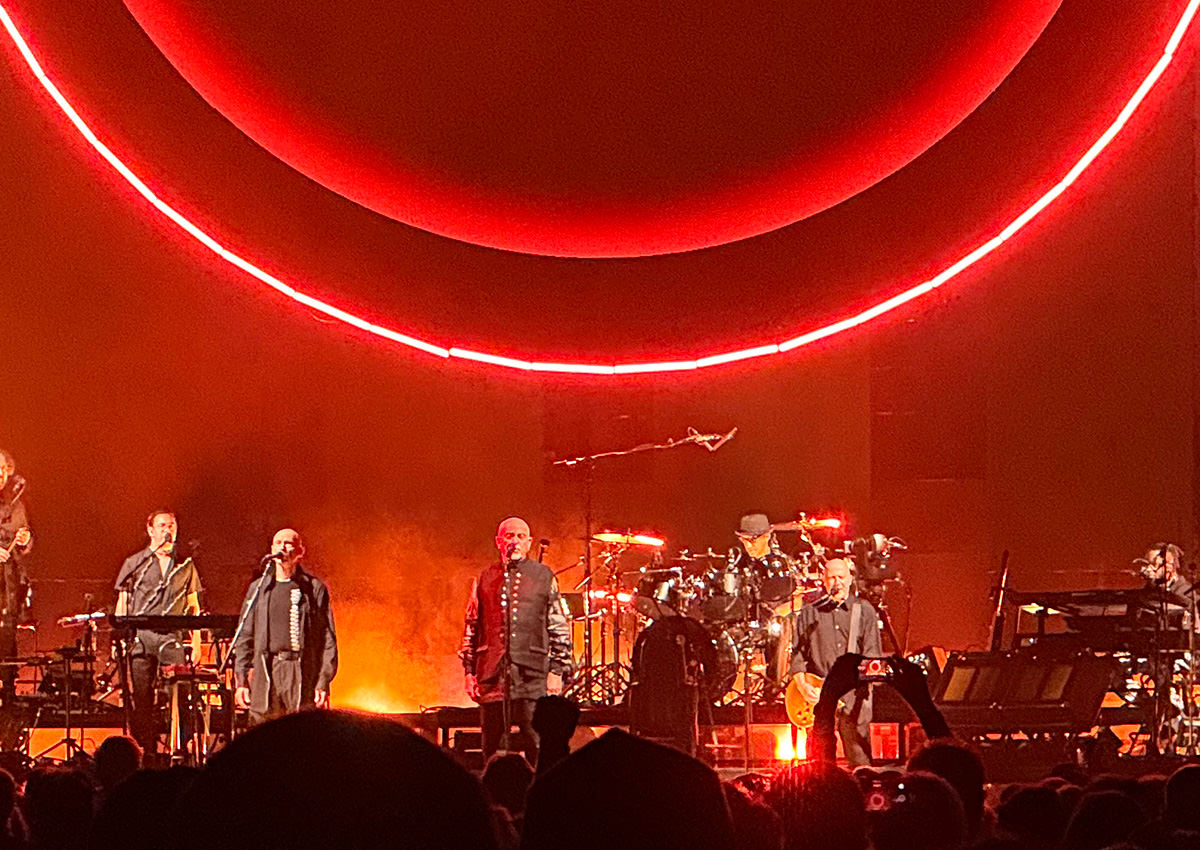 Peter Gabriel singing in front of a blood red background.