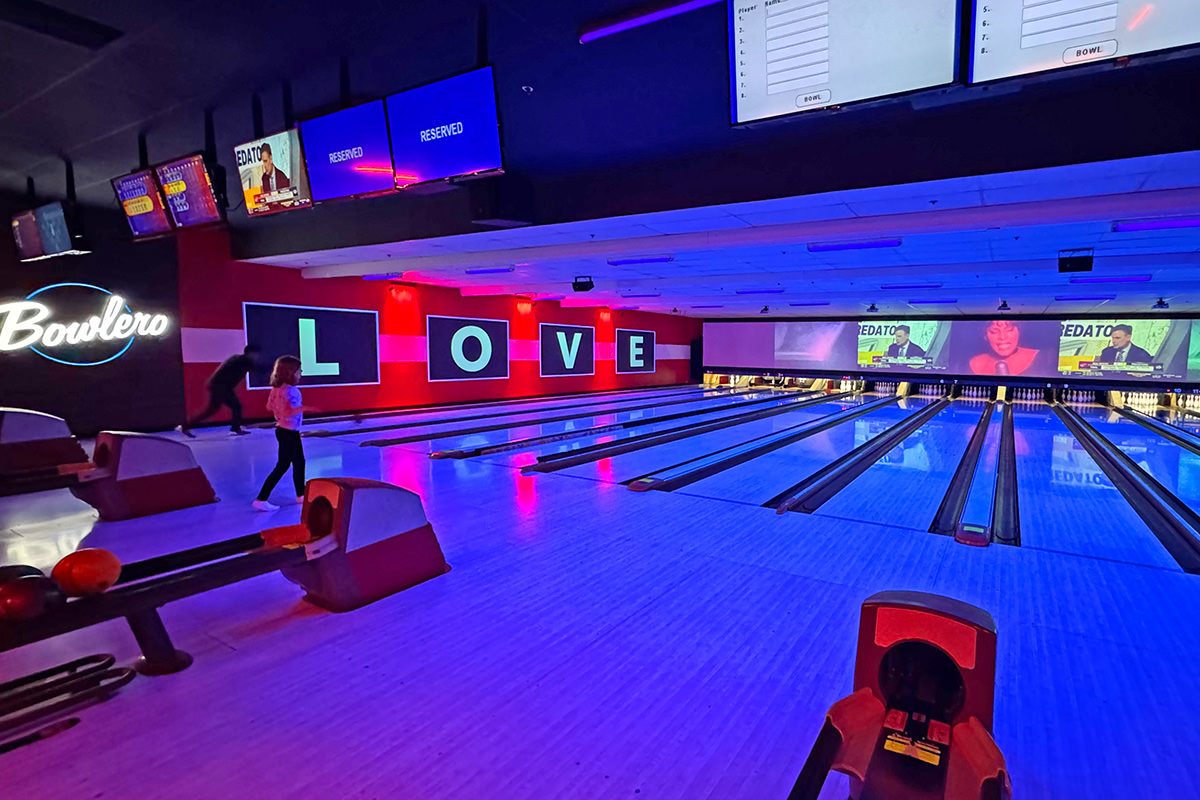 The funky Bowlero lanes with saturated, colorful lights and music videos playing.