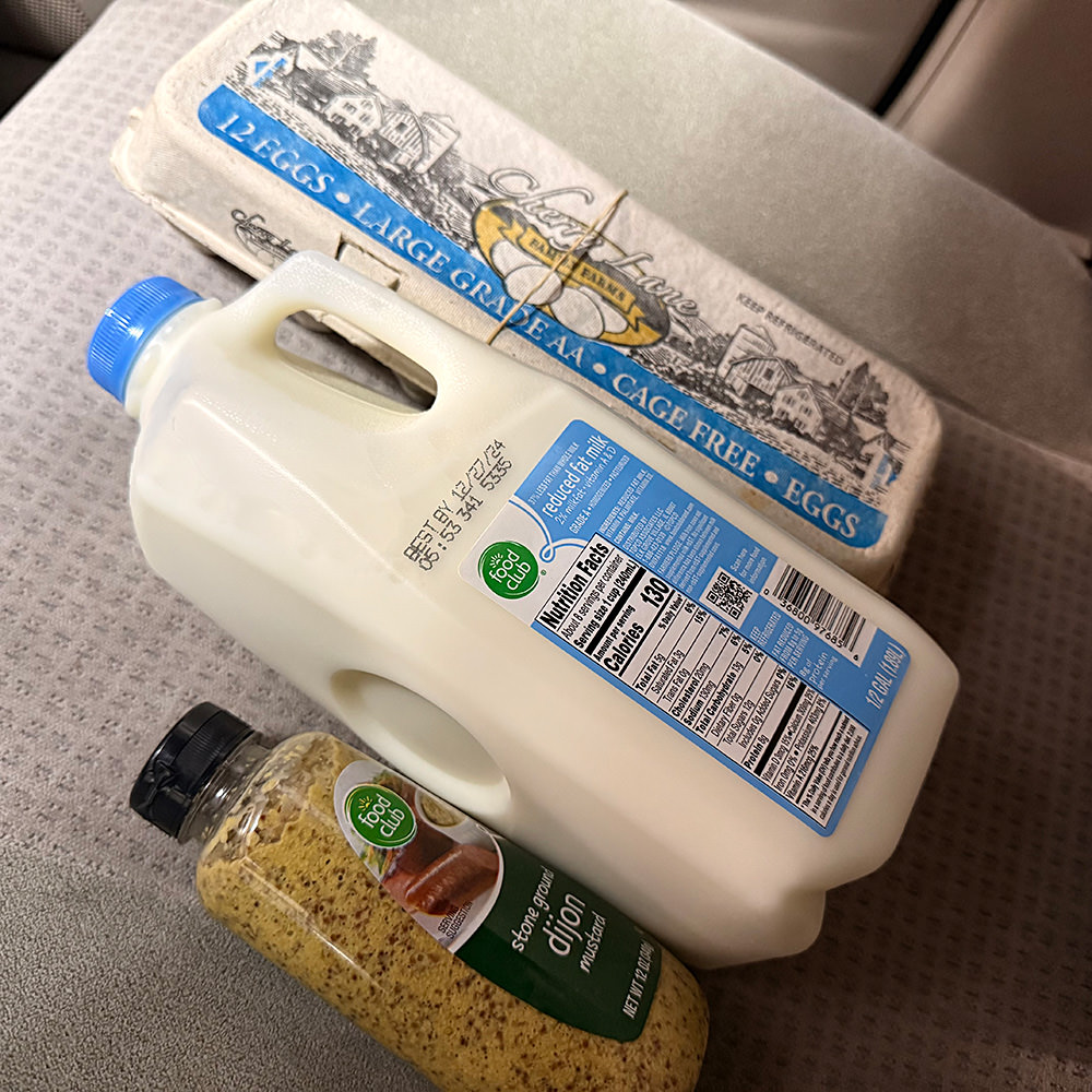 Eggs with a rubber band around them, a half-gallon of milk, and a bottle of stone-ground Dijon mustard.