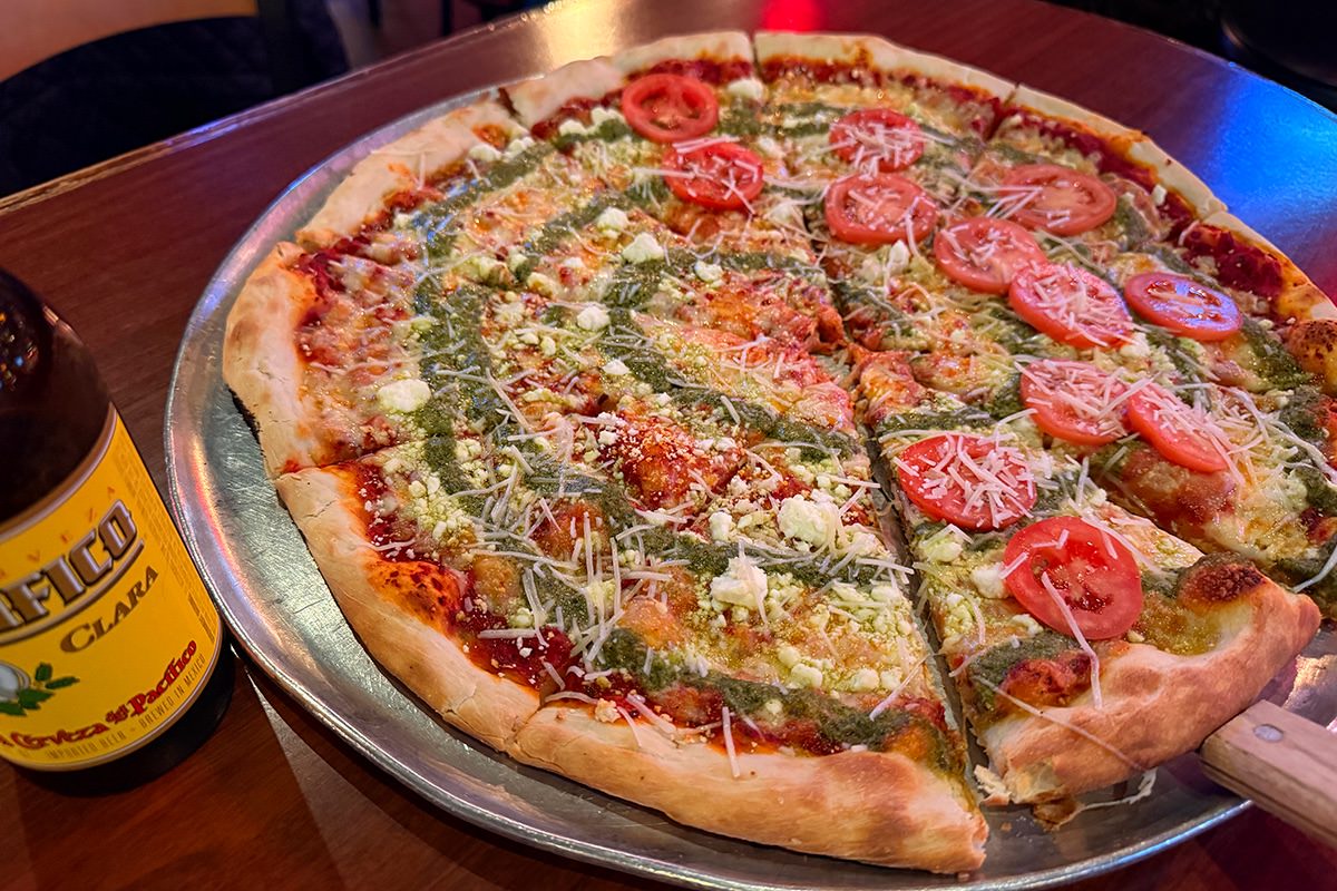 A Pacifico Beer and a large pizza with pesto, feta, and tomatoes.