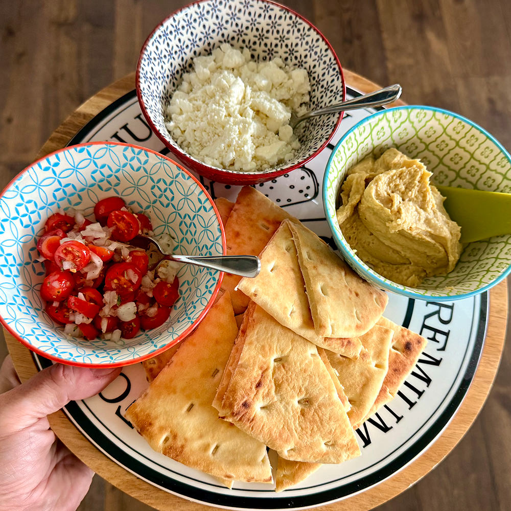 A plate of pretty hummus, herbed tomatoes & onions, feta, and toasted naan.